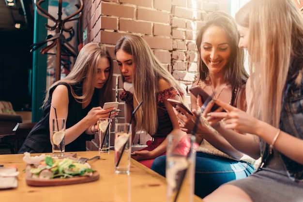 Cztery Uśmiechniętej Studentki Siedzącej W Kawiarni Na Czacie I Za Pomocą Telefonów Komórkowych