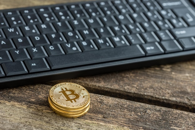 Zdjęcie cztery złote monety bitcoin w pobliżu czarnej klawiatury komputera nad drewnianym stołem z miejscem na kopię