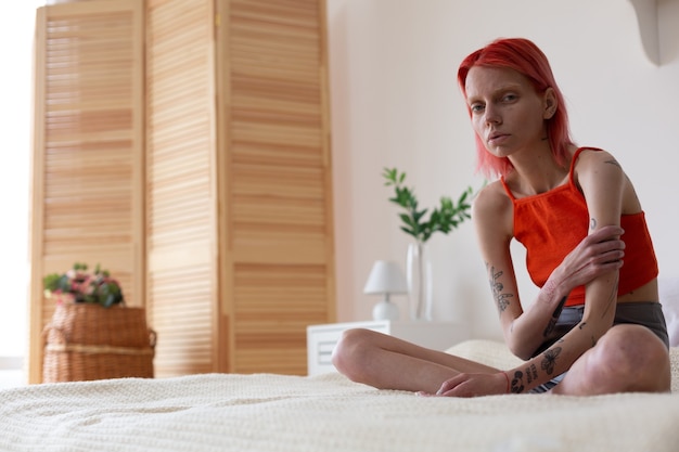Czuć Się Nędznie. Rudowłosa Anorektyczka Z Tatuażami Na Ramionach Czuje Się Nieszczęśliwa Siedząc Na łóżku