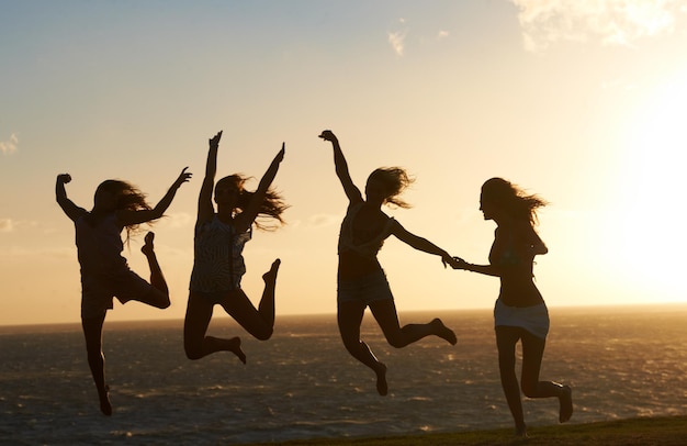 Czuję się na szczycie świata Sylwetka grupy dziewczyn na plaży, która świetnie się bawi skacząc dookoła