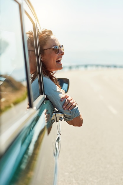 Zdjęcie czuję się wolny na otwartej drodze przycięte zdjęcie atrakcyjnej kobiety wystającej z okna samochodu podczas podróży samochodem