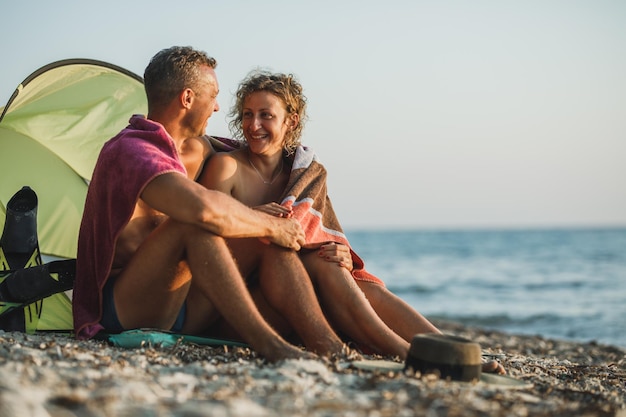 Czuła młoda para spędzająca dzień na plaży i podziwiająca zachód słońca zawinięta w koc.