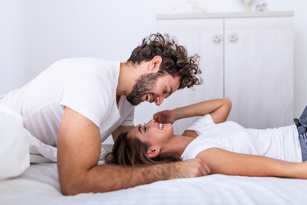 Czule młoda atrakcyjna para dzieli romantyczny moment w sypialni w domu. Szczęśliwa młoda para przytulanie i uśmiechając się leżąc na łóżku w sypialni w domu.
