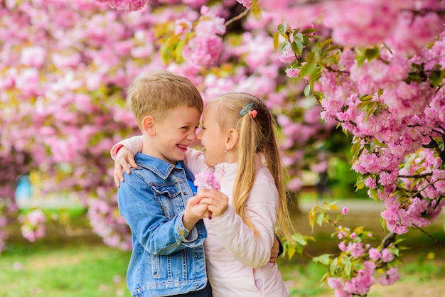 Czułe uczucia miłosne Para dzieci na kwiatach sakury na tle drzewa Mała dziewczynka cieszy się wiosennymi kwiatami Daje jej wszystkie kwiaty Zaskakując ją Dzieci cieszą się różowym kwiatem wiśni Romantyczne dzieci
