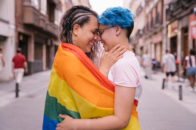 Czuły pocałunek między dwiema kobietami owiniętymi gejowską flagą.