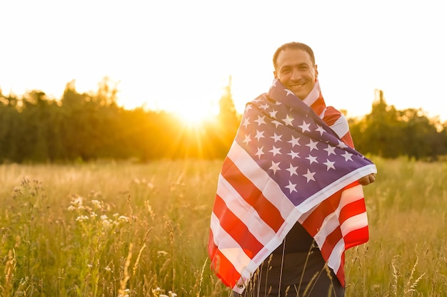 Czwarty lipca. Patriotyczny mężczyzna z narodową flaga amerykańską w polu. Młody człowiek z dumą macha amerykańską flagą. Dzień Niepodległości.