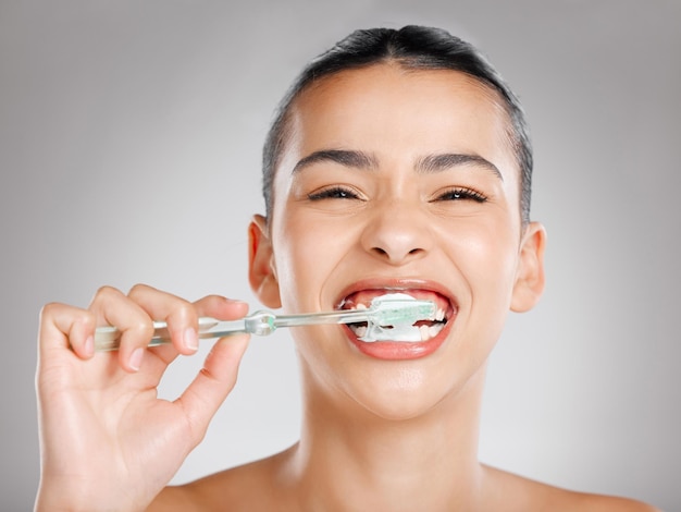 Czy twój dentysta dumny Studio ujęcia atrakcyjnej młodej kobiety szczotkującej zęby na szarym tle?