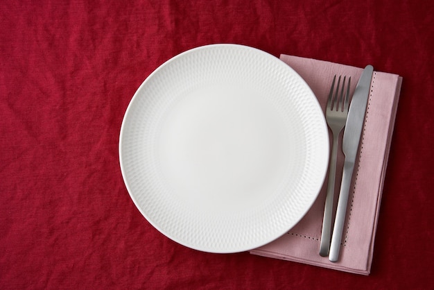 Czyść pusty biały talerz, widelec i nóż na jasnoczerwonym obrusie tekstylnym z żurawiny na stole