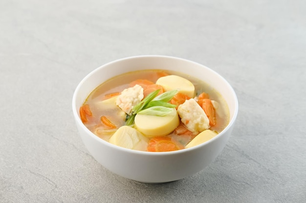 Czysta zupa z jajkiem tofu, marchewką i klopsikami z krewetek, podawana w białej misce na szarym tle
