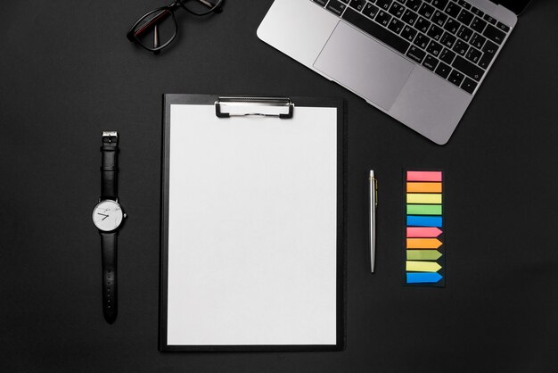 Czysty biały arkusz papieru z bezpłatną przestrzenią do kopiowania, laptopem, zegarkiem i długopisem na czarnym tle.