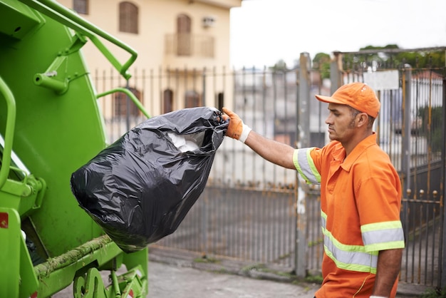 Zdjęcie czyszczenie gospodarki odpadami i śmieci z ciężarówką z mężczyzną w mundurze rzucanie czarnej torby na zewnątrz na ulicy miejskiej usługa robocza i śmiecie z poważną osobą pracującą dla sanitarnej lub zbierania brudu