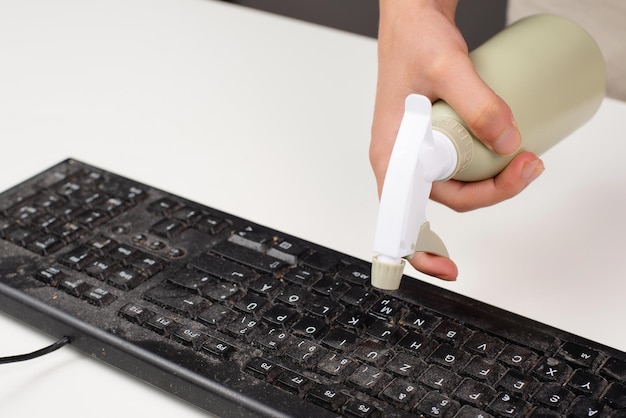 Czyszczenie klawiatury komputera w biurowej wodzie w sprayu za pomocą butelki z rozpylaczem, zakurzonych, brudnych elektronicznych prac domowych