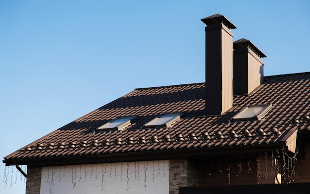 Zdjęcie dach wykonany z brązowej metalowej dachówki na tle błękitnego nieba. na dachu znajduje się komin domowy oraz świetliki.