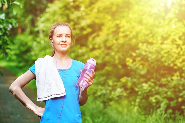Dama fitness z butelką i ręcznikiem wody po uruchomieniu treningu w letnim parku