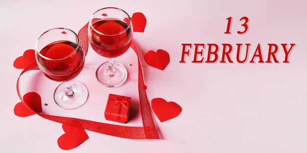 Zdjęcie data kalendarza na jasnym tle z dwiema lampkami czerwonego wina czerwone pudełko i serca 13 lutego