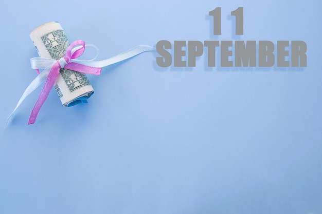 Data kalendarza na niebieskim tle z zwiniętymi banknotami dolarowymi przypiętymi niebieską i różową wstążką z miejscem na kopię 11 września to jedenasty dzień miesiąca
