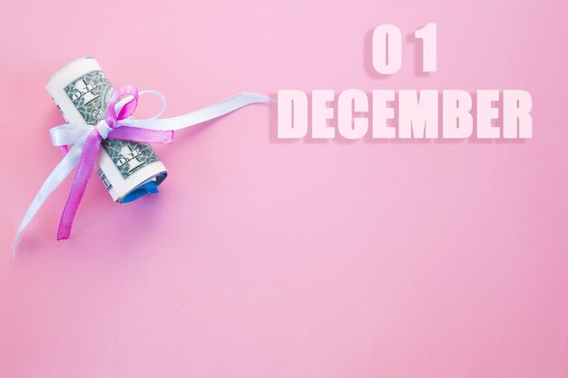Data kalendarza na różowym tle z zwiniętymi banknotami dolarowymi przypiętymi różową i niebieską wstążką z miejscem na kopię 1 grudnia jest pierwszym dniem miesiąca