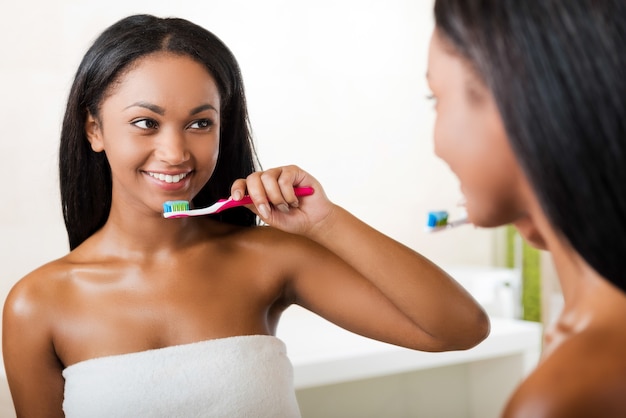 dbanie o jej zęby. piękna młoda afrykańska kobieta myjąca zęby i uśmiechająca się