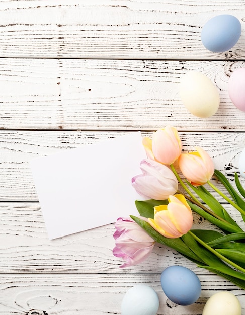 Zdjęcie dekoracja domu na wakacje wielkanocne tło z jajkami tulipanami i pustą kartą do makiety na białym drewnianym tle widok z góry płaski lay