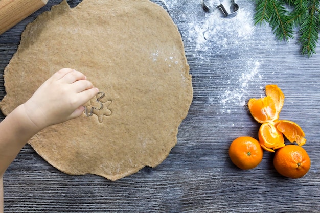 Dekoracje noworoczne i świąteczne na drewnianej powierzchni z mandarynkami i choinką Ręce małego dziecka tworzą formy do gotowania pierników w postaci mężczyzny