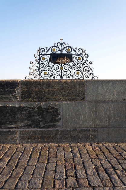 Dekoracyjna krata z brązową statuą Jana Nepomucena na Moście Karola Praga Czechy słoneczny dzień