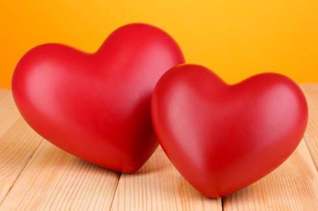 Dekoracyjne czerwone serca na drewnianym stole na pomarańczowym tle