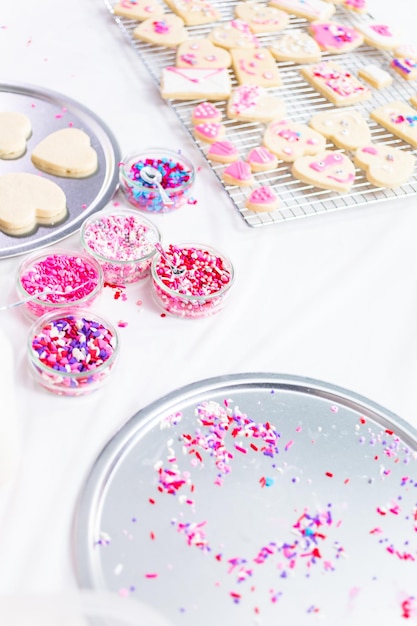 Dekorowanie cukrowych ciasteczek w kształcie serca z królewskim lukrem i różową posypką na Walentynki.