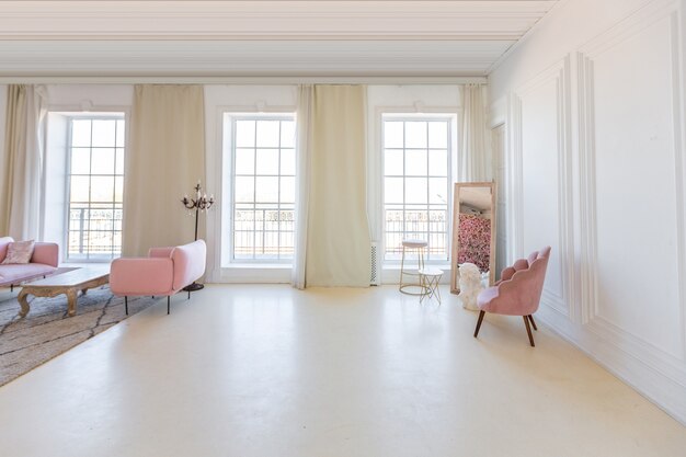 Delikatne i przytulne jasne wnętrze salonu z nowoczesnymi stylowymi meblami w pastelowym różowym kolorze i białymi ścianami z sztukaterią w świetle dziennym