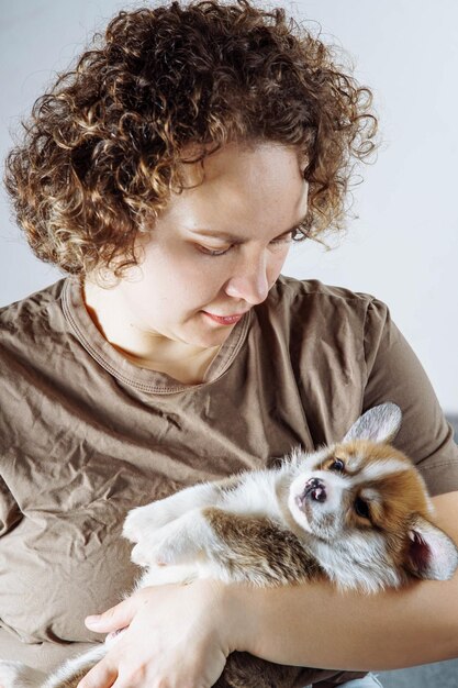 Zdjęcie delikatność i troska młoda kobieta w ciemno beżowej bawełnianej koszulce kochająco przytula słodkiego małego walijskiego szczeniaka corgi