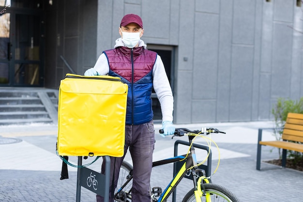 Delivery Man stojący z żółtym plecakiem termicznym do dostawy żywności w pobliżu wejścia do domu z pustą przestrzenią do kopiowania wklej.