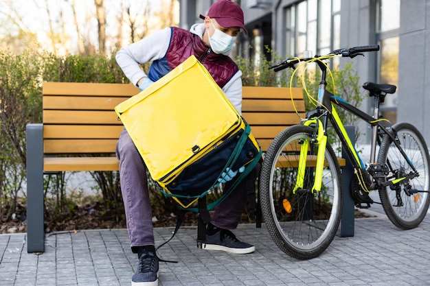 Zdjęcie delivery man stojący z żółtym plecakiem termicznym do dostawy żywności w pobliżu wejścia do domu z pustą przestrzenią do kopiowania wklej.