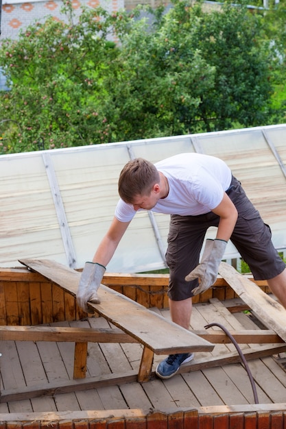 Demontaż dachu. Pracownik zdejmuje stare deski z dachu, dom jest remontowany.