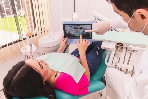 Zdjęcie dentysta analizuje rentgen dentystyczny z pacjentem leżącym na krześle dentystycznym
