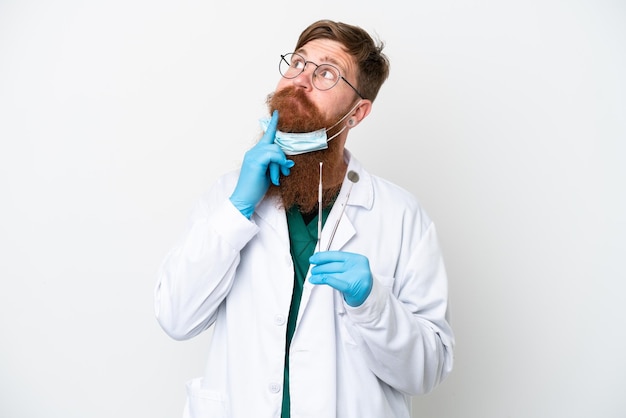 Dentysta czerwonawy mężczyzna trzymający narzędzia odizolowane na białym tle i patrzący w górę
