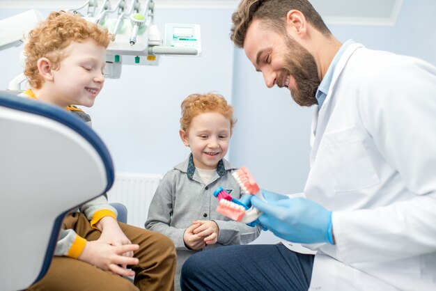Dentysta dziecięcy pokazujący chłopcom jak myć zęby na sztucznej szczęce w gabinecie stomatologicznym