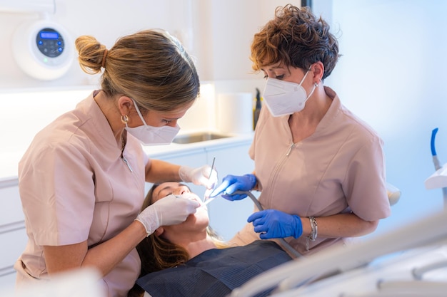 Dentysta i asystent badający usta pacjenta leżącego na krześle kliniki