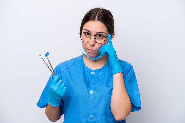 Dentysta kaukaska kobieta trzyma narzędzia na białym tle myśląc o pomyśle