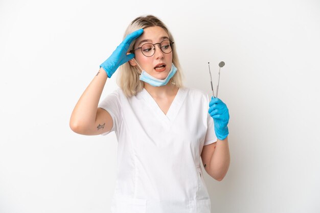 Dentysta kaukaska kobieta trzymająca narzędzia na białym tle, wykonująca gest zaskoczenia, patrząc w bok