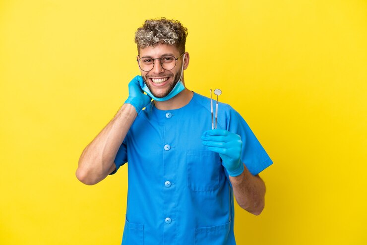 Zdjęcie dentysta kaukaski mężczyzna trzymający narzędzia izolowane na żółtym tle śmiejąc się