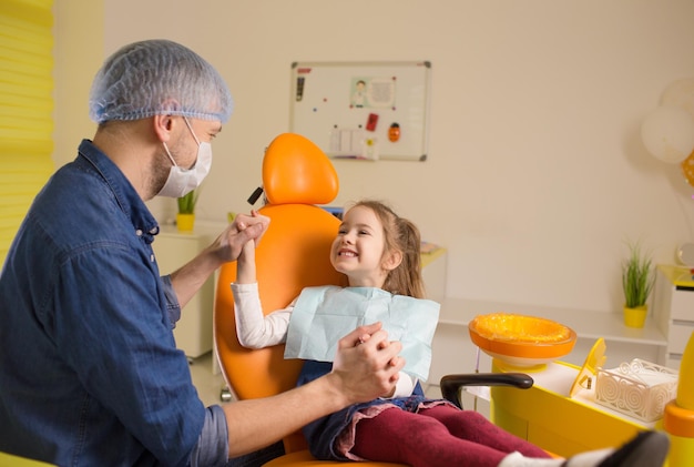 Dentysta mężczyzna trzyma za ręce małej pacjentki, która wspiera ją przed rozpoczęciem leczenia stomatologicznego
