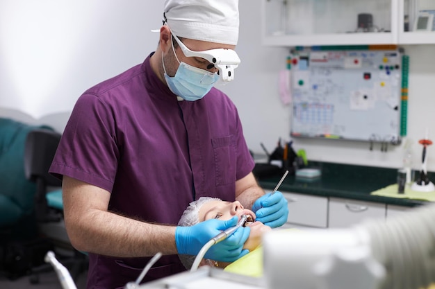 Dentysta ortodonta używający sprzętu dentystycznego do leczenia próchnicy młodej pacjentki w klinice dentystycznej