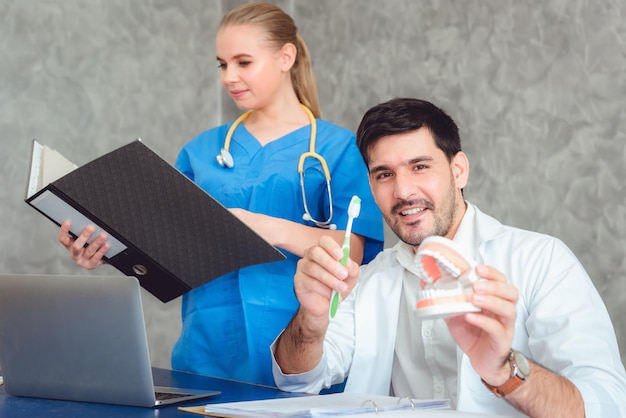 Zdjęcie dentysta pokazujący protezy i szczoteczkę do zębów przez kolegę trzymającego plik na stole