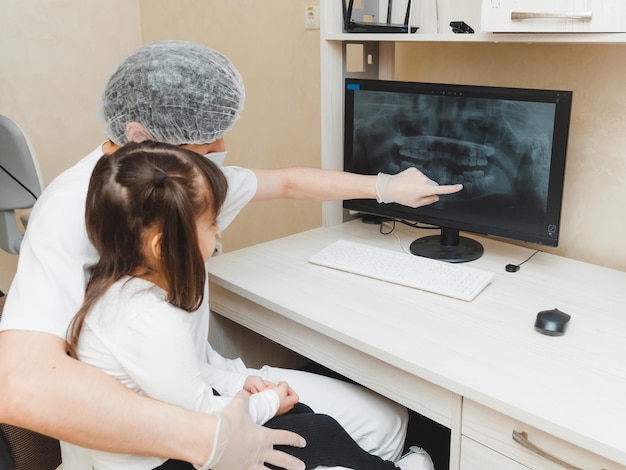 Dentysta pokazuje pacjentce dziewczynce zdjęcie rentgenowskie zębów na komputerze