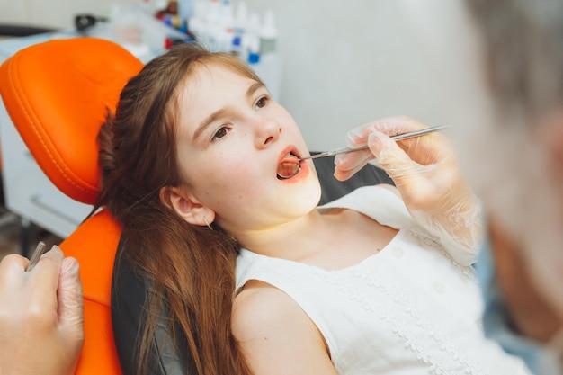 Dentysta przeprowadza badanie na uroczej dziewczynce Mała dziewczynka siedzi w gabinecie dentystycznym