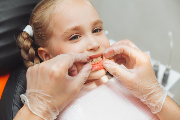 Dentysta przeprowadza badanie na uroczej dziewczynce Mała dziewczynka siedzi w gabinecie dentystycznym