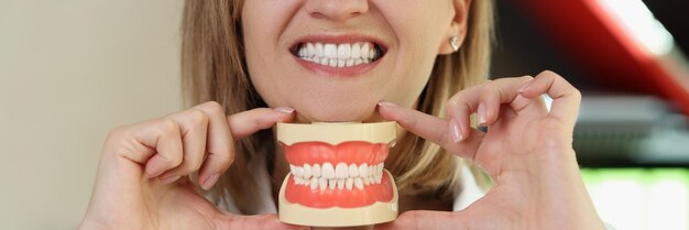 Dentysta uśmiecha się i pokazuje plastikowe szczęki w dłoniach kobieta stomatolog trzymająca sztuczne zęby