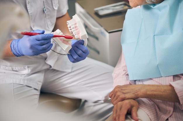 Dentysta w białym mundurze trzymającym model implantu dentystycznego w celu wyjaśnienia korpusu zęba