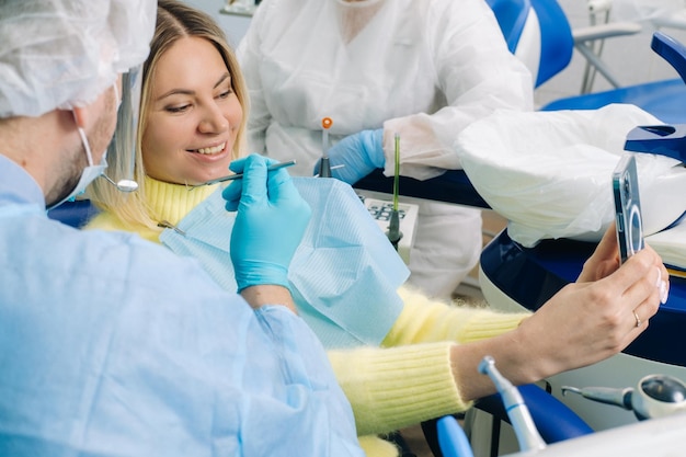 Zdjęcie dentysta w masce ochronnej siedzi obok pacjenta i podczas pracy robi sobie zdjęcie selfie