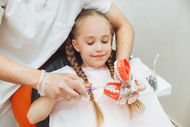 Zdjęcie dentysta w mundurze medycznym pokazuje małej dziewczynce, jak prawidłowo myć zęby na modelu szczęki koncepcja stomatologii