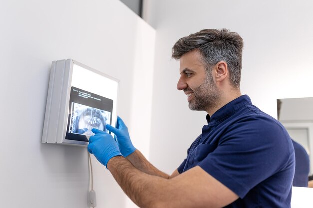 Dentysta w niebieskich fartuchach, badający prześwietlenie zębów na ekranie komputera Dentyści, którzy chcą prześwietlić zęby na monitorze w klinice dentystycznej